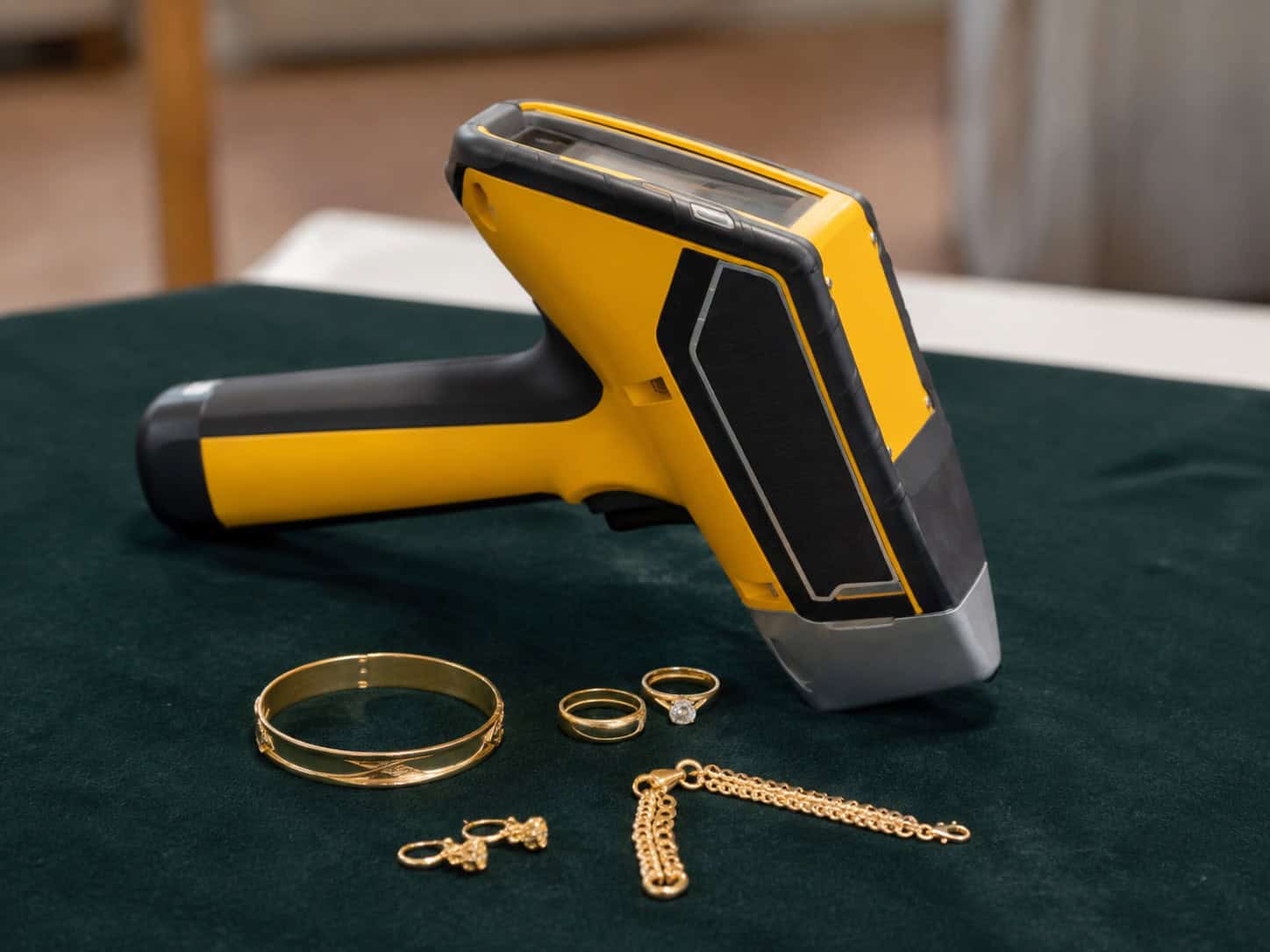 Handheld XRF analyser on a valuation table beside a gold bangle, rings, earrings and a chain waiting to be tested