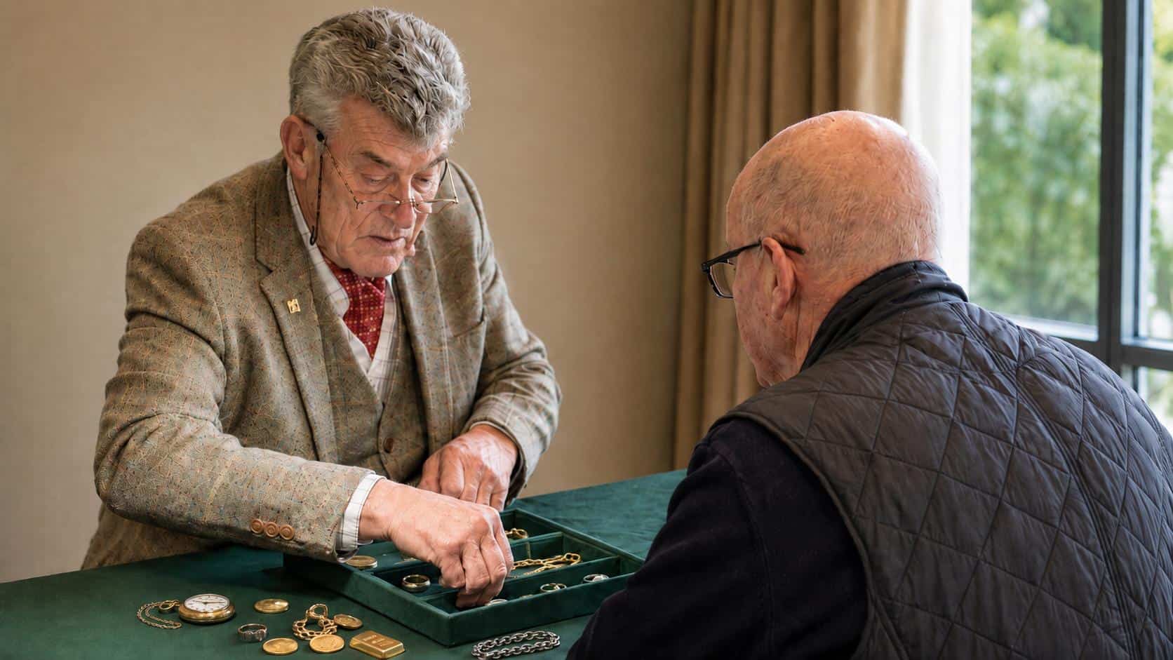 Valuer examining a customer's jewellery, coins and pocket watch across a valuation table