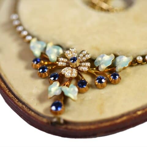 Close-up of the necklace centrepiece: sapphires and seed-pearl flowers with carved opalescent leaves, in its velvet-lined case