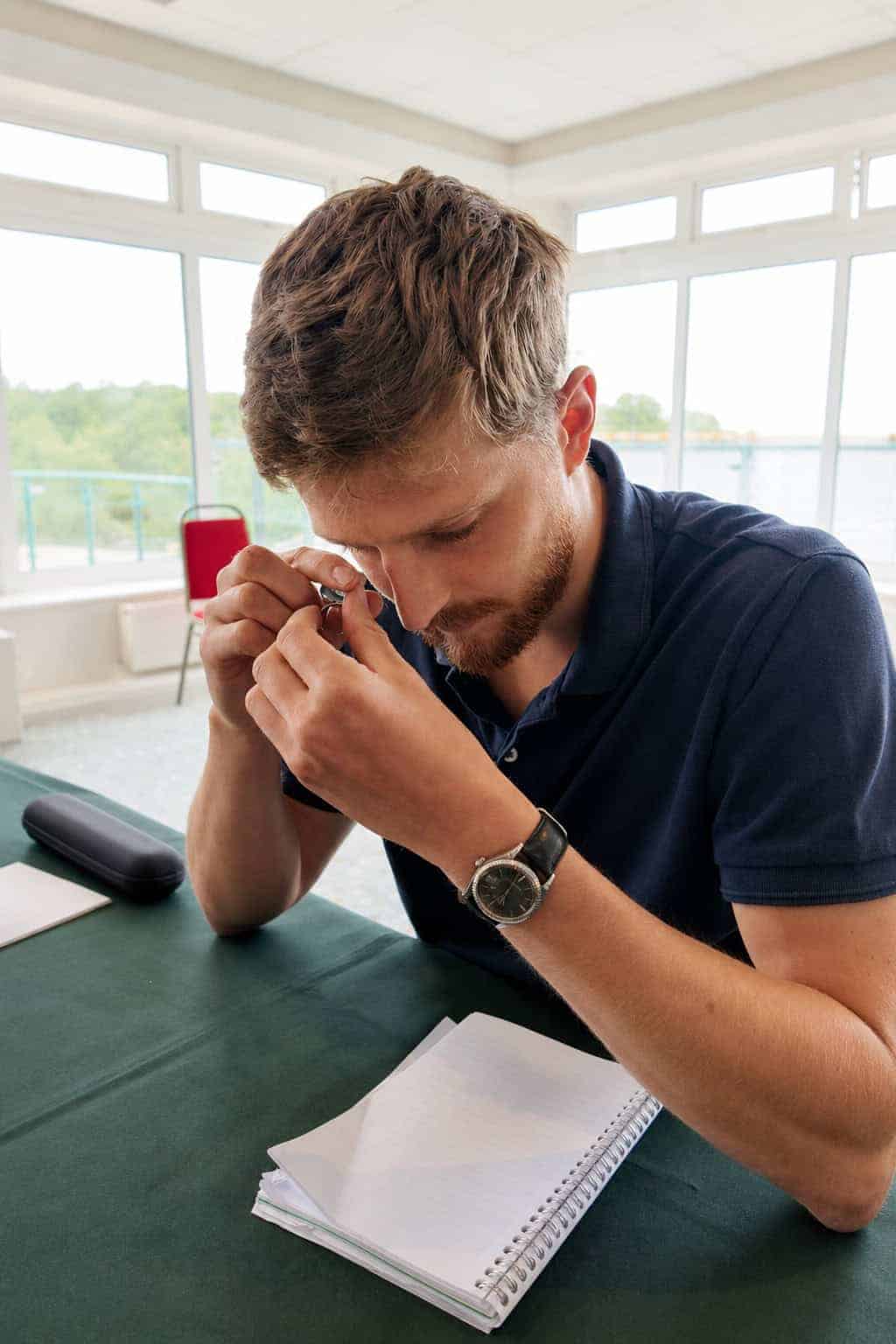 Samuel inspecting a ring with a jeweller's loupe at a roadshow valuation table